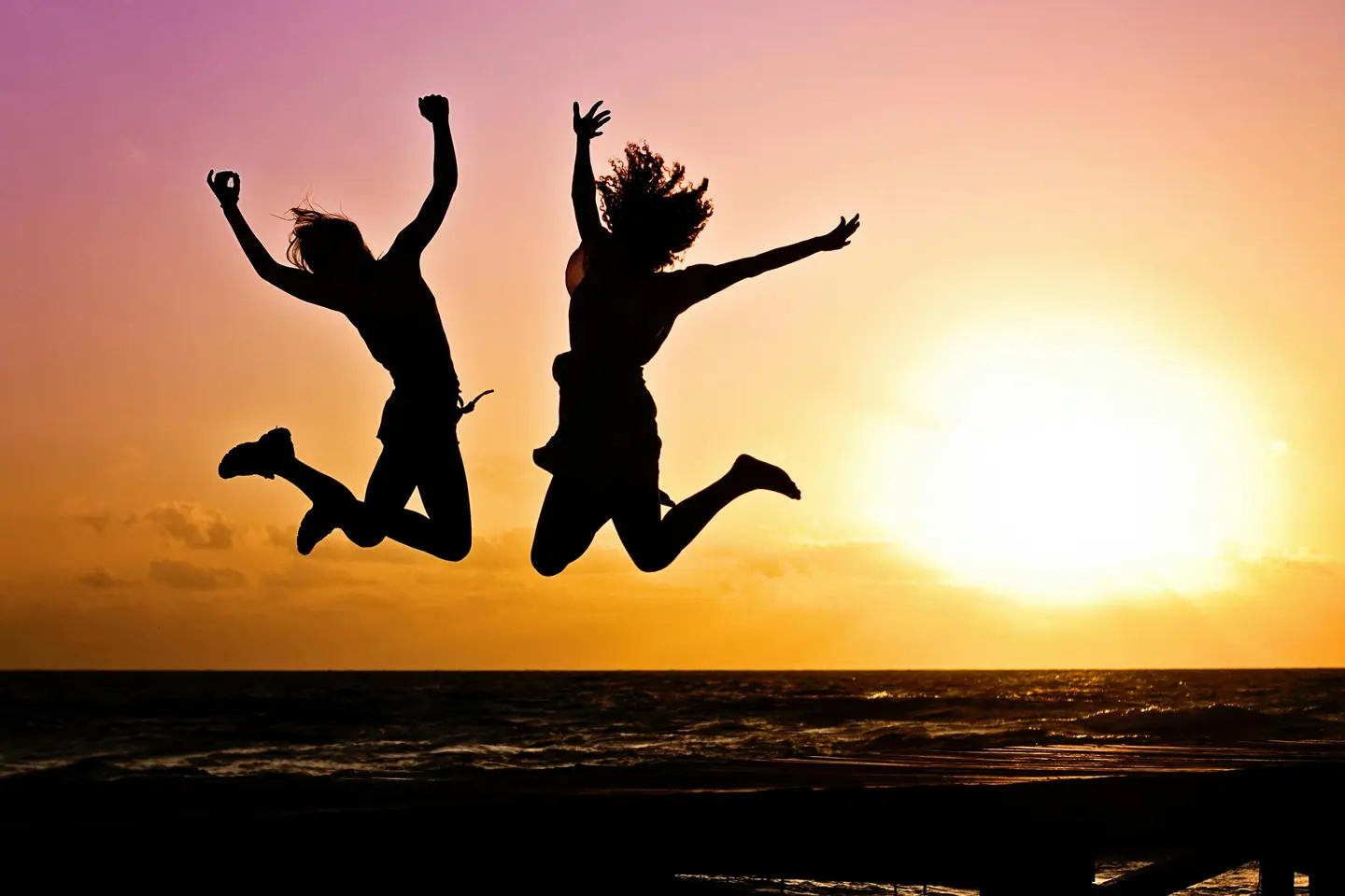 Two people jumping on a beach at sunset