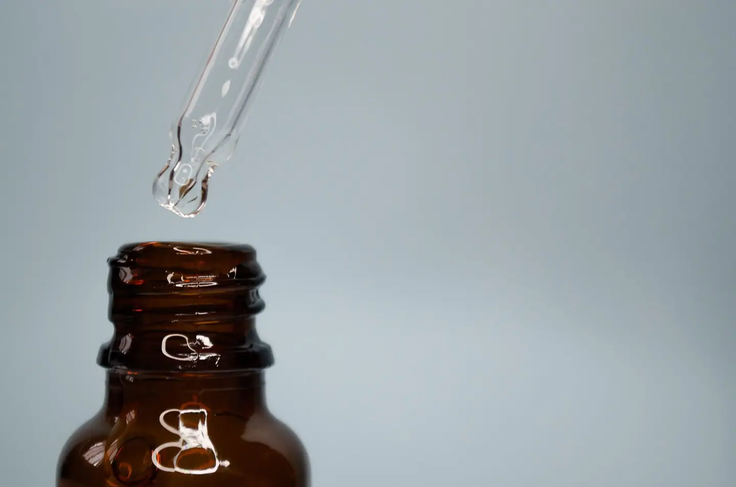 A clear drop forming at the tip of a dropper above an amber bottle
