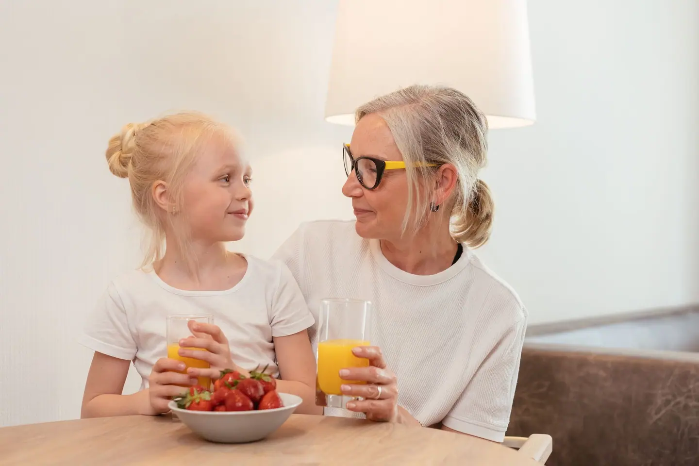 A grandmother and granddaughter sharing juice and strawberries at the table