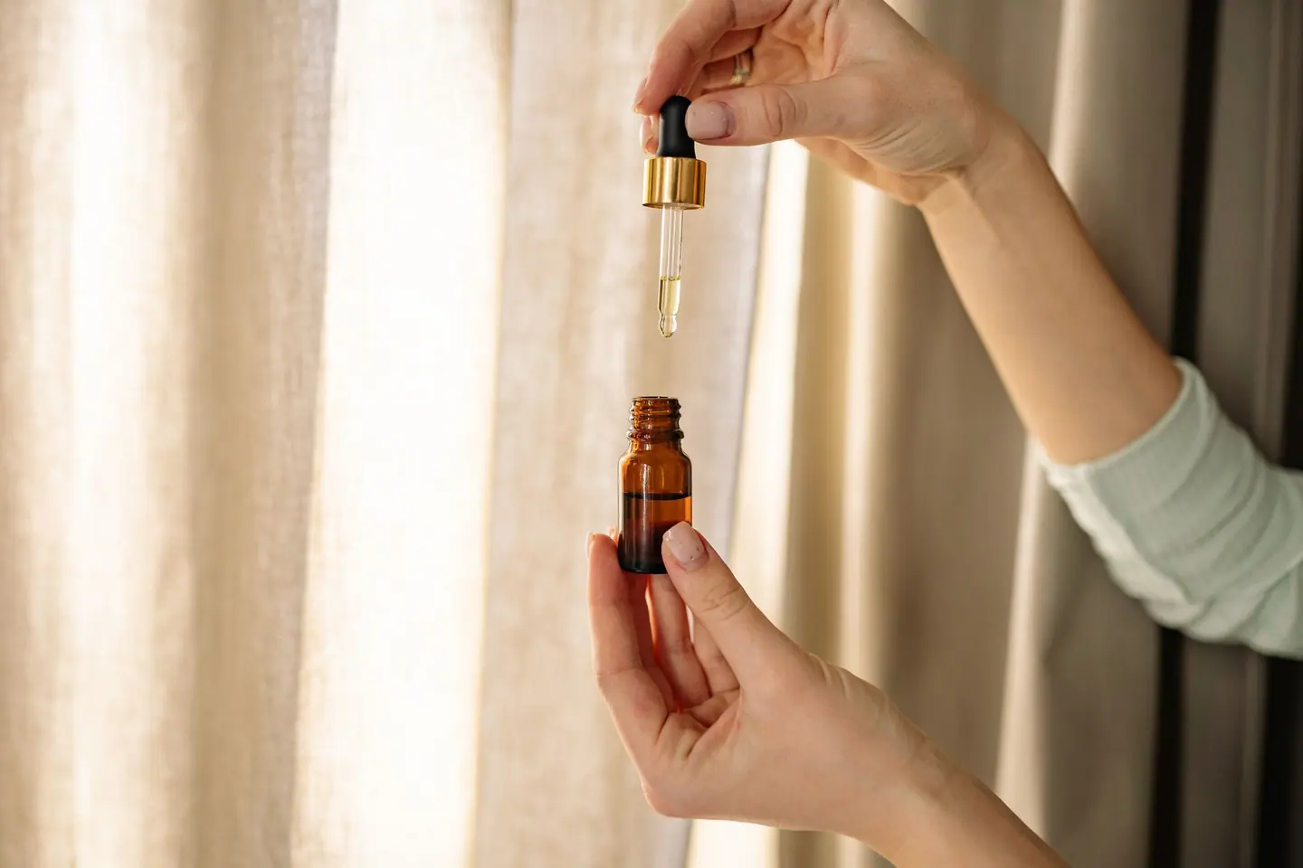 A hand drawing oil into a dropper from a small amber glass bottle